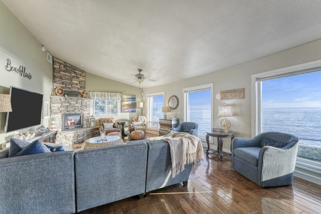 Photo of living space with comfortable fabric couches and chairs, large flat screen TV, and fireplace - all overlooking the Pacific at Day Dreamin'