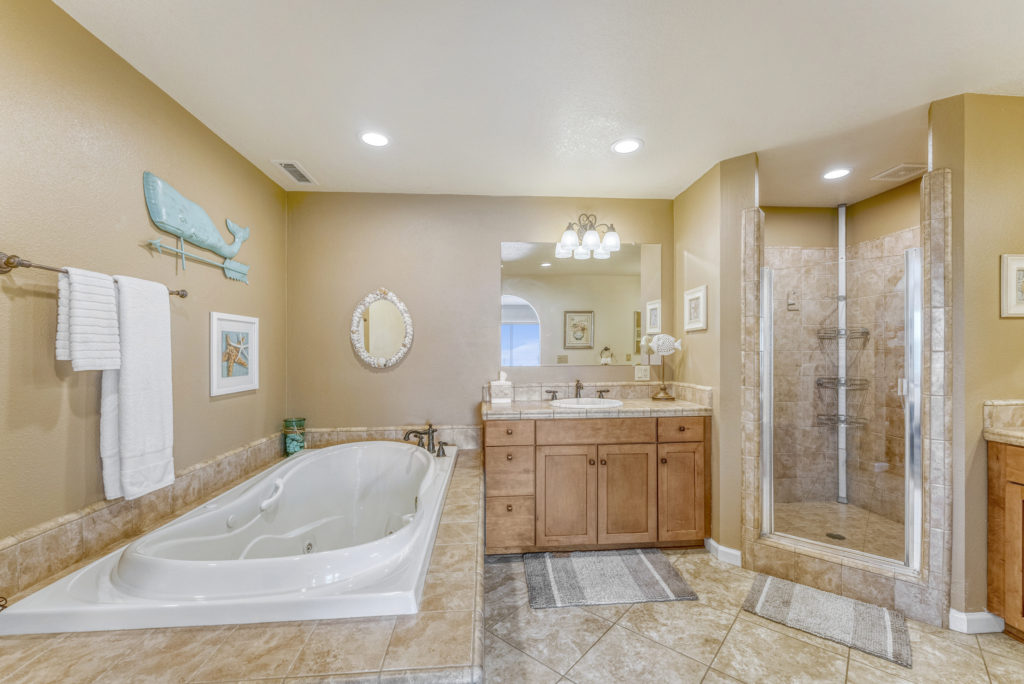 Photo of master bathroom featuring large soaking tub, two vanities, shower - all with tile flooring & countertops