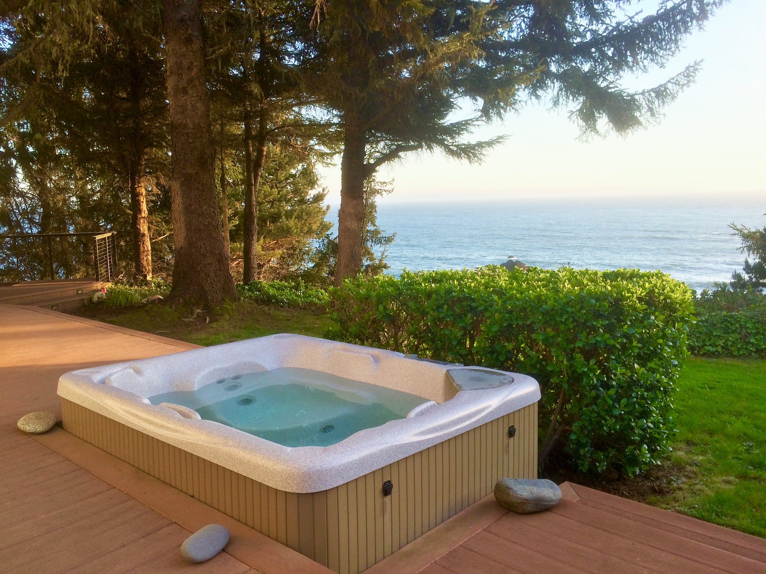 Photo of large hot tube on the deck with greenery and ocean view
