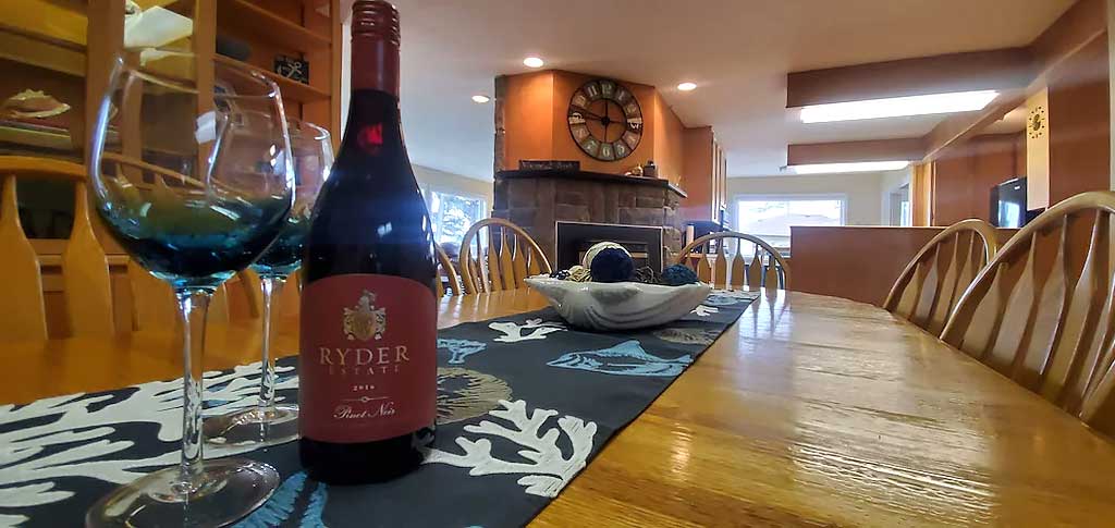 Photo of dining room table with sine bottle and glasses in the foreground and kitchen in the background