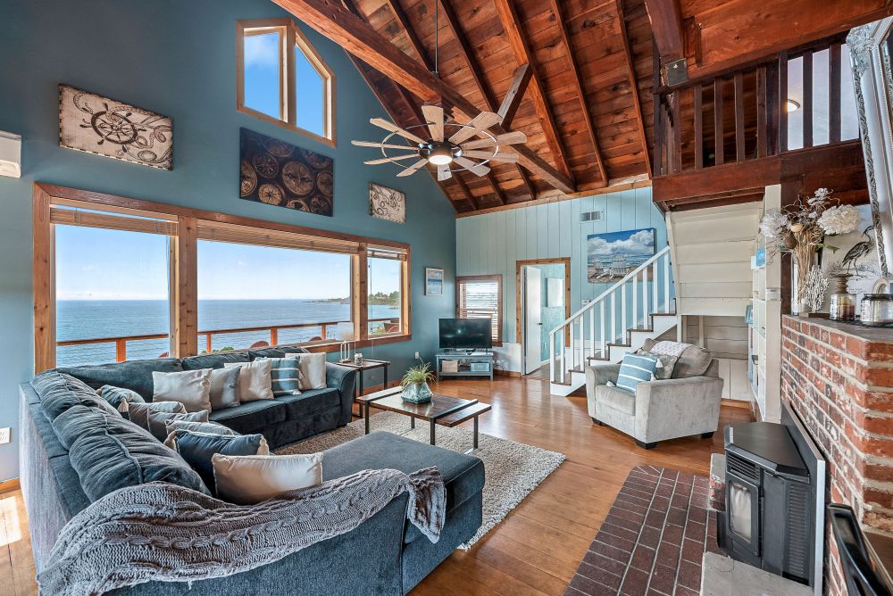 Photo of great room with hardwood floors, wood burning stove, ceiling fan, vaulted wood paneled ceiling and large oceanview windows
